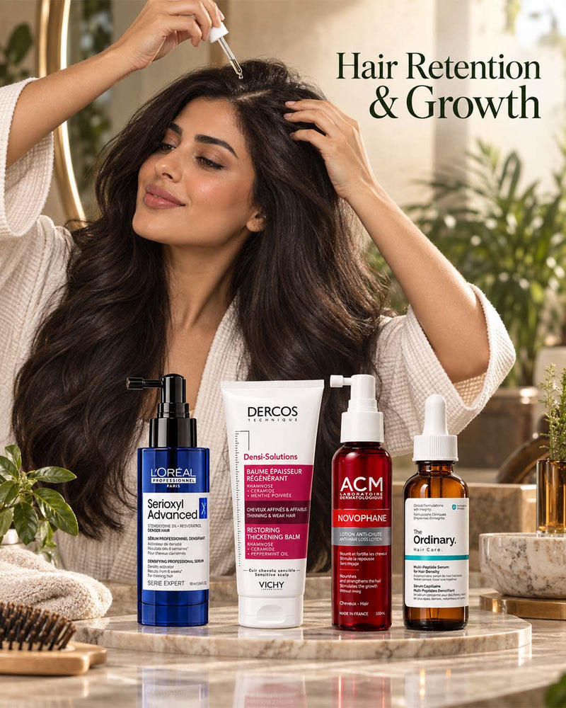 Woman applying scalp serum with a dropper surrounded by hair growth treatments including L'Oréal Professionnel Serioxyl Advanced Denser Hair Serum, ACM Novophane Anti-Hair Loss Lotion, and The Ordinary Multi-Peptide Serum for Hair Density.